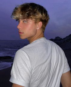 a young man standing on top of a beach next to the ocean at night time