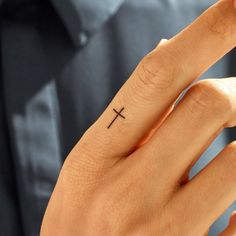 a person's hand with a small cross tattoo on the middle finger and fingers