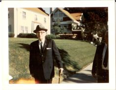 an old man in a suit and hat is walking down the sidewalk with his cane