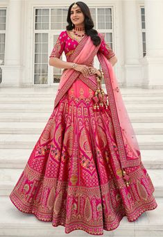 a woman in a pink and gold lehenga standing on steps with her hands on her hips