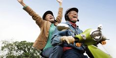 two people riding on the back of a green scooter with their arms in the air