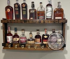 a wooden shelf filled with different types of liquors on top of a white wall