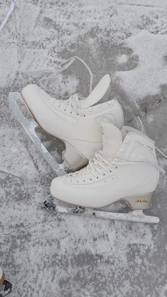 a pair of white ice skates sitting on top of snow covered ground next to each other