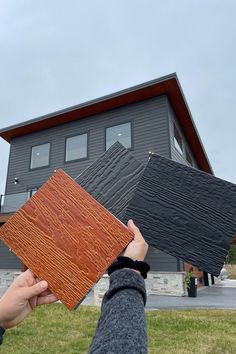 two people holding up some wood in front of a large gray house on a cloudy day