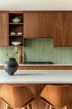 two wooden stools sit in front of a kitchen counter with green backsplash