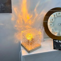 a white clock sitting on top of a table next to a yellow light in the shape of a cube