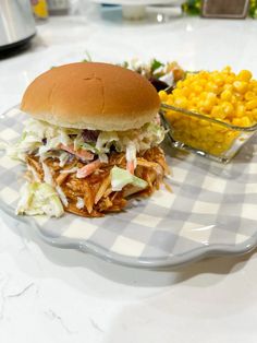 a pulled pork sandwich with cole slaw and corn on the cob sits on a plate