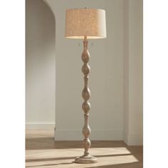 a floor lamp with a beige shade on it's side and a white wall in the background