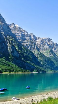 three boats are sitting on the shore of a lake in front of some mountain peaks