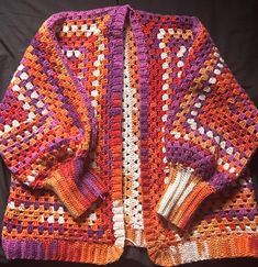 an orange and purple crocheted sweater laying on top of a black tablecloth