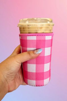 a woman's hand holding a pink and white checkered cup with gold lid