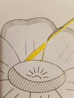 a yellow thread is being sewn on a white piece of fabric with a flower in the background