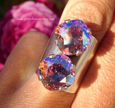 two rings with different colored stones on them sitting in front of some pink and purple flowers