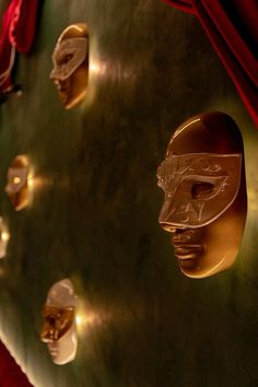 gold masks are on display in front of red velvet drapes and wall - hangings