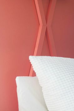 a white pillow sitting on top of a bed next to a pink wall