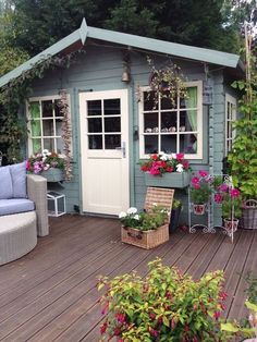 a wooden deck with chairs and potted plants next to a small shed filled with flowers