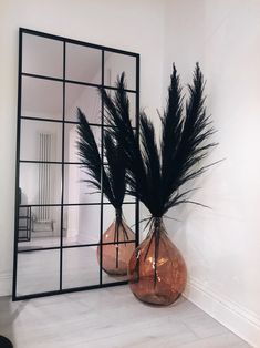 two vases with black feathers in front of a mirror