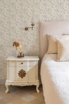 a white bed sitting next to a night stand on top of a wooden dresser in a bedroom