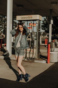 a woman standing in front of a gas station with her hand on her head and looking at the camera