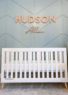 a white crib in front of a blue wall with the name hudson above it