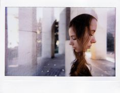 a woman with long hair standing in front of a wall and looking into the distance