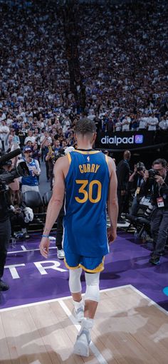 a basketball player walking on the court in front of an arena full of people and photographers