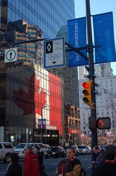 many people are crossing the street in front of tall buildings with canadian flags on them