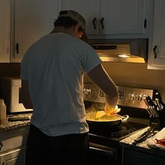 a man is cooking in the kitchen with his hands on the stove top and he is wearing a white t - shirt