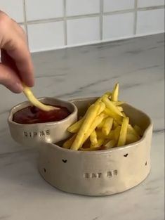 a person dipping fries into a bowl with ketchup and mustard on the side