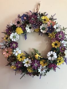 a floral wreath hanging on the wall with purple, yellow and white flowers in it