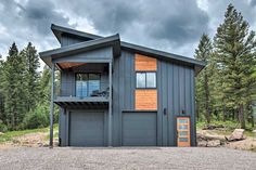 a two story building with an attached balcony and garage on the top floor, surrounded by pine trees