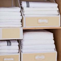 folded towels are stacked on wooden shelves in a room with white linens and brown bins