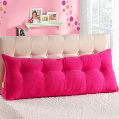 a pink pillow on top of a bed in a room with polka dot wallpaper