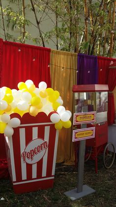 a popcorn bucket filled with yellow and white balloons sitting on top of a grass covered field