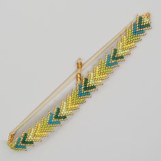 a yellow and blue beaded bracelet with an arrow charm hanging from it's end