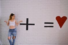 a woman standing in front of a white brick wall with the word love painted on it