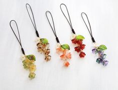 four different colored flowers are hanging from black cords on a white tablecloth, one is made out of glass beads and the other has leaves