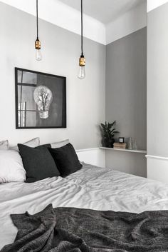 a bed with white sheets and black pillows in a bedroom next to two hanging lights