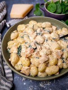 a bowl filled with pasta and spinach covered in sauce next to a plate of cheese