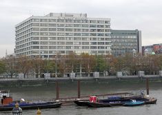 two boats are docked in the water near a large building and other buildings on either side of the river