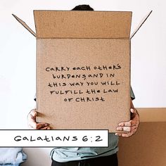 a person holding up a cardboard sign with the words galaians 6 2