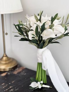 a bouquet of white flowers sitting on top of a wooden table next to a lamp