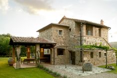 a stone house with an outdoor patio and table in the front yard, surrounded by greenery