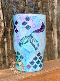 a blue and purple cup sitting on top of a wooden table in front of trees