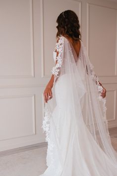 a woman in a wedding dress with a long veil on her head and back, standing next to a white wall