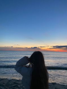 a woman standing on top of a sandy beach next to the ocean at sunset or dawn