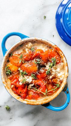 a pot filled with lots of food on top of a white counter next to a blue pan