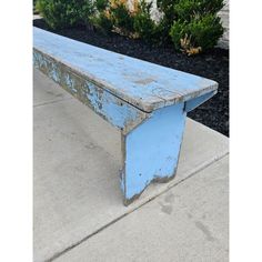 an old blue bench sitting on the side of a sidewalk next to bushes and shrubbery