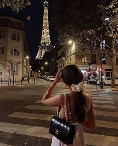 a woman is standing on the street in front of the eiffel tower at night