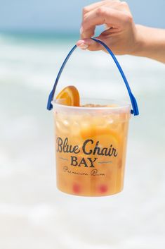 a person holding up a bucket filled with oranges and ice cream on the beach